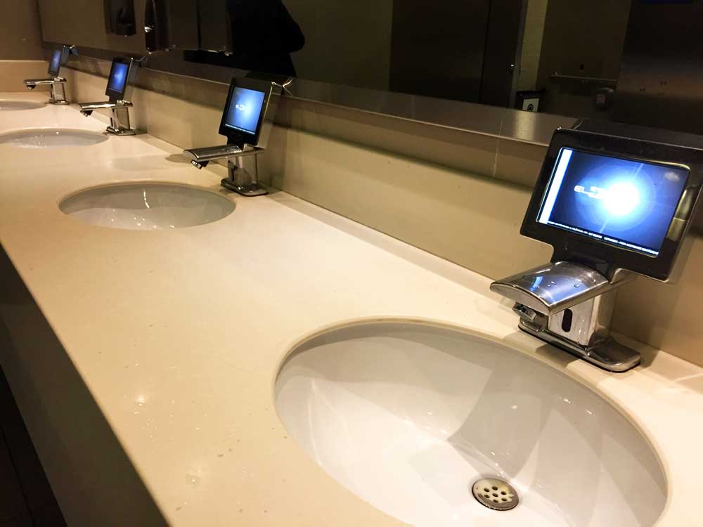 Kleine Bildschirme an den Waschbecken in den Toilettenräumen am Flughafen in Bogota.