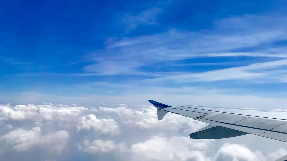 Tragflaeche eines Flugzeugs ueber den Wolken vor blauem Himmel